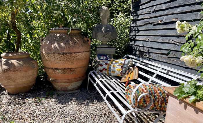 A white bench in a sunny garden surrounded by planted terracotta pots