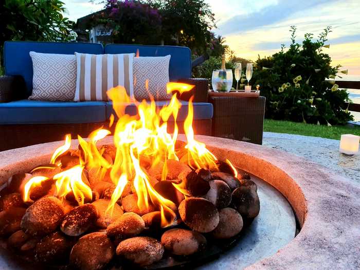 A firepit in the foreground with a sofa, and side table with wine in the background