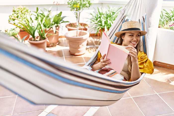 Smiling woman reading in a hammock with terracotta pots in the background