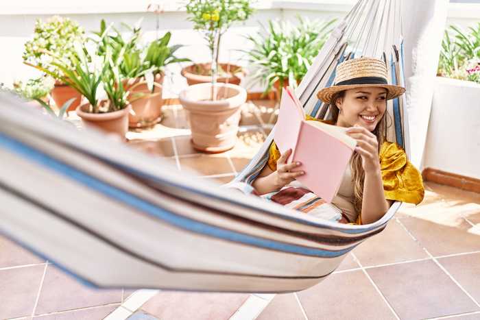 Smiling woman reading in a hammock with terracotta pots in the background